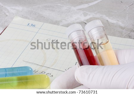 Hand holding test tubes in front of a laboratory notebook.