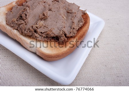 Liver pate on a piece of toasted white bread on a white plate.