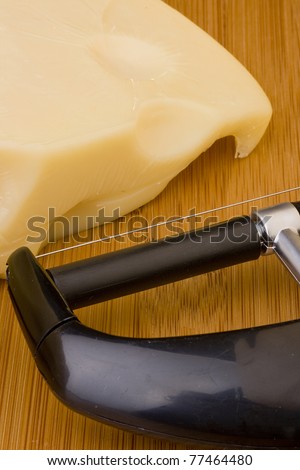 Swiss cheese slice and Cheese slicer on a wood desk.