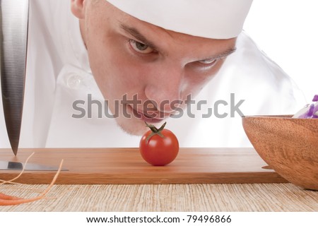 The young chef in chef\'s hat is considering a tomato.