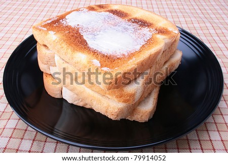 Toasted white bread with butter on a black plate.