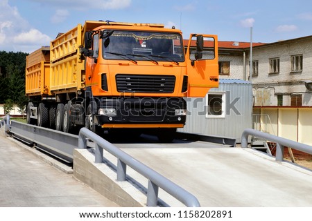 orange truck with grain is weighed on the scales in the grain storage area. Truck scales