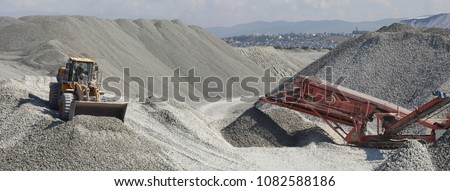 Wheel loader excavator and mobile crusher against the background of crushed stone hills, panorama. Mining industry. Heavy equipment.