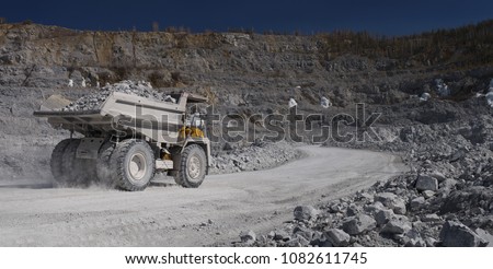 Heavy dump-body truck loaded with limestone ore moves along the road in a quarry, back view, panorama. Mining industry. Heavy equipment.
