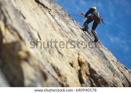 Climber climbs on the rock wall against a blue sky. Climbing gear. Climbing equipment.