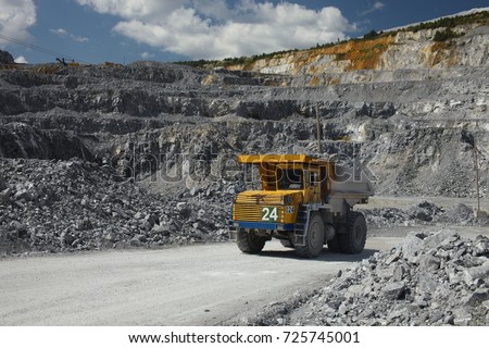 Large multi-toned mining truck in a limestone quarry on the background of blue sky with clouds. Quarry equipment. Mining industry.