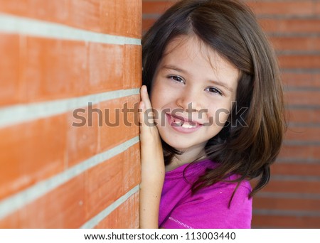 Portrait of an adorable little girl behind a brick wall playing peek a boo
