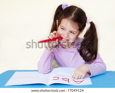 Little girl writing alphabet in a copybook and thinking