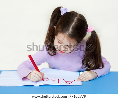 Little girl writing alphabet in a copybook at a desk