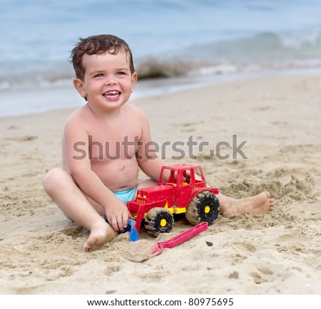 Smiling kid playing on a beach with a red toy car
