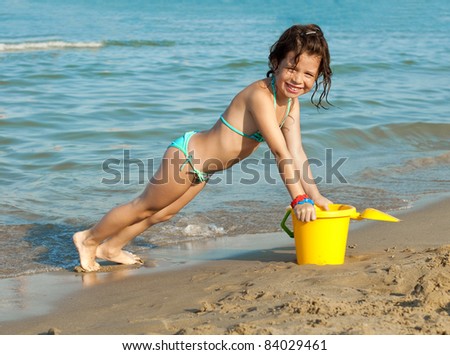 Smiling girl playing with a yellow pail on the beach