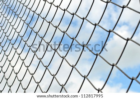 Chain link fence looking up against cloudy blue sky