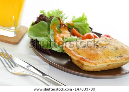 A meal of chicken pie with salad and a glass of orange juice