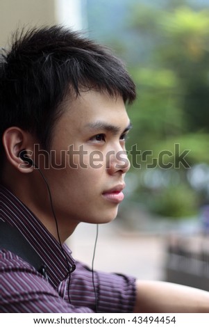 A young Asian man listening to music at a balcony
