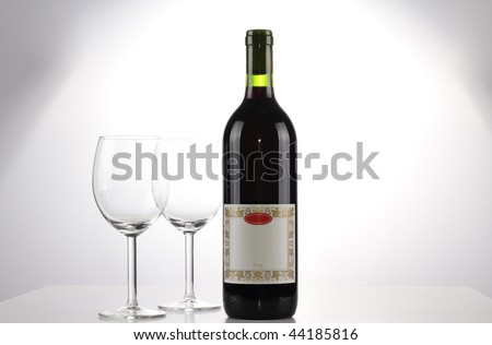 A bottle of red wine with a blank label and two emtpy wine glasses