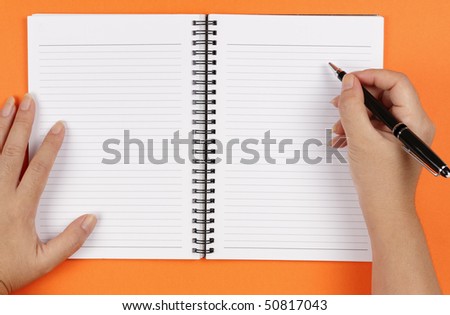 A pair of hands, a pen and a notebook on an orange background