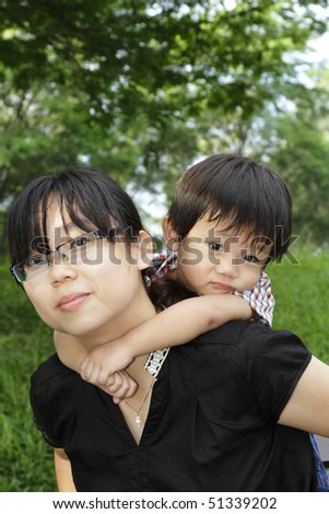 An Asian mother giving her son a  piggyback ride in a public park