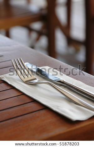Knife and fork on serviette on a wooden table, taken at an outdoor restaurant, with copy space