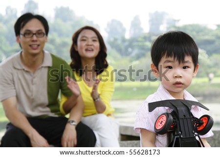 An Asian boy playing with his toy as his parents watch on