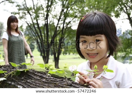 A curious Asian girl examining a creeper plant as her mother watches