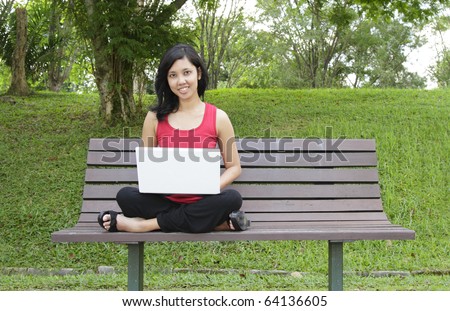 An Asian woman with a laptop sitting on a bench