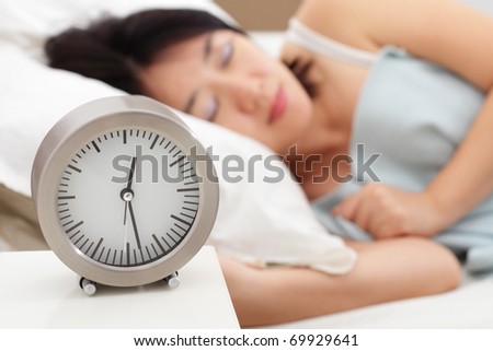 A table clock and a woman sleeping in the background