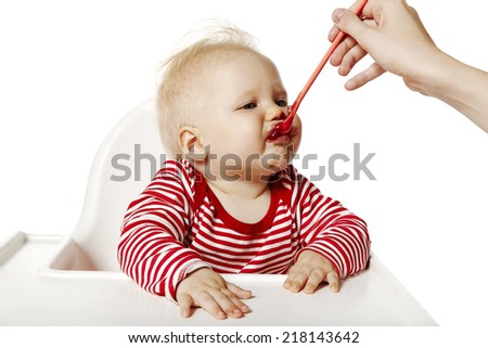 Studio shot of baby sitting on chair and eating dinner. Isolated on white background.