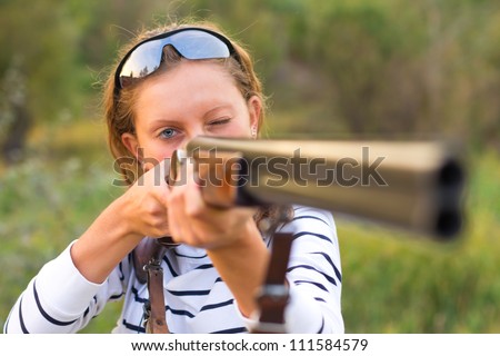 A young girl with a gun for trap shooting and shooting glasses aiming at a target