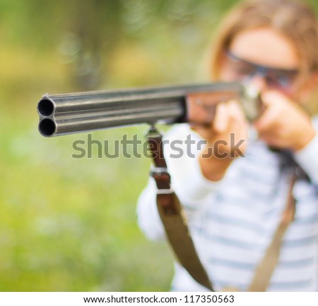 A young girl with a gun for trap shooting and shooting glasses aiming at a target. Short depth of field, focus on the barrel