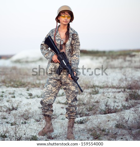 Young beautiful female soldier dressed in a camouflage with a gun in the outdoor