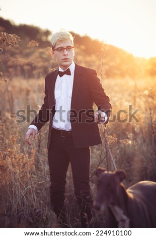 Young attractive man in suit and tie with a greyhound dog in autumn outdoors. He keeps the dog on the leash.