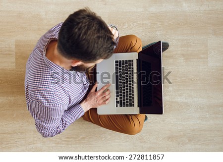 Top view of young man sitting on the floor and working with a laptop