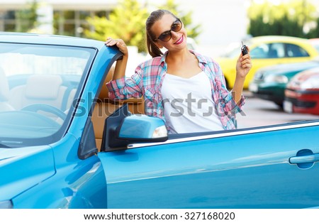 Young pretty woman in sunglasses standing near convertible with keys in hand - concept of buying a used car or a rental car