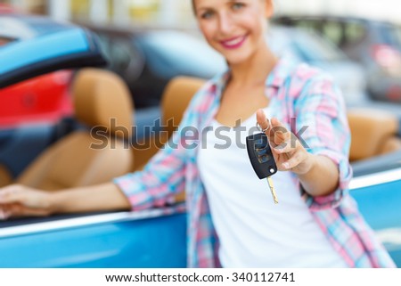 Young woman standing near a convertible with keys in hand - concept of buying a used car or a rental car