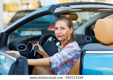 Young pretty woman sitting in a convertible car with the keys in hand - concept of buying a used car or a rental car