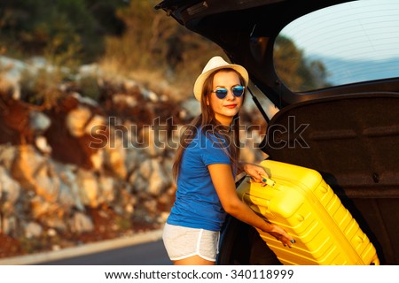 Young woman loading luggage into the back of car parked alongside the road