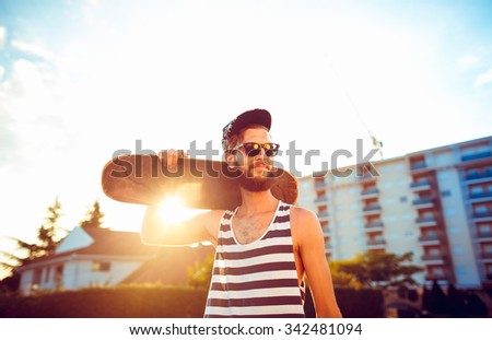 Young stylish man in sunglasses with a skateboard on a street in the city at sunset light