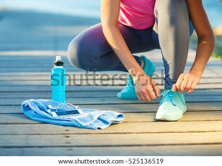 Running shoes - woman tying shoe laces. Closeup of female sport fitness runner getting ready for jogging outdoors on waterfront in late summer or fall