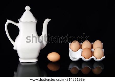 White porcelain teapot with six eggs in a white porcelain egg tray, one of the eggs at the side of the tray.