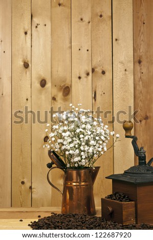 antique coffee grinder beans and copper pitcher with flowers on wood background