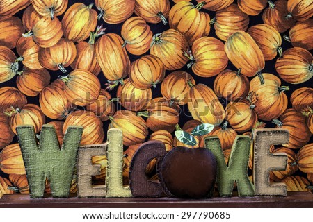 wood craft welcome sign in front of black cloth imprinted with orange pumpkins