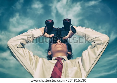 Young business man looking through binocular, low angle view