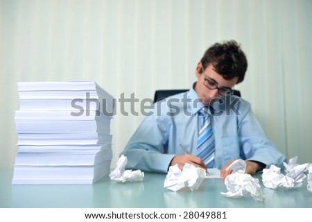 Young businessman writing at a desk with big stack of papers