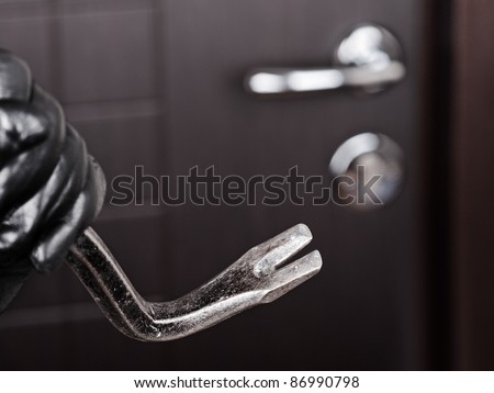 Crime scene - criminal thief or burglar hand in gloves holding metal crowbar break opening home door lock