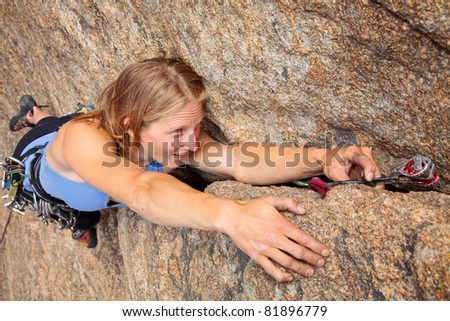 Woman rock climber placing piece of gear