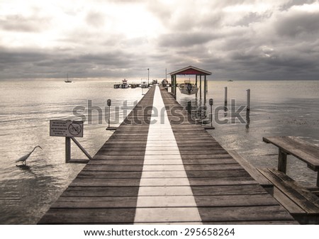 A thick white line shows the way down the middle of a wooden jetty to the edge of the pier where there is a small wooden shed and a hanging speed boat on early morning in San Pedro in Ambergris Caye