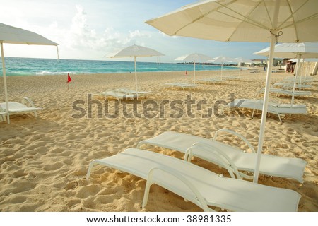 Beach in harmony with a peaceful zen-like spirit made up of white lounge chairs and white umbrellas on white sand with a glimpse of the turquoise water of a cancun beach under a bright sky