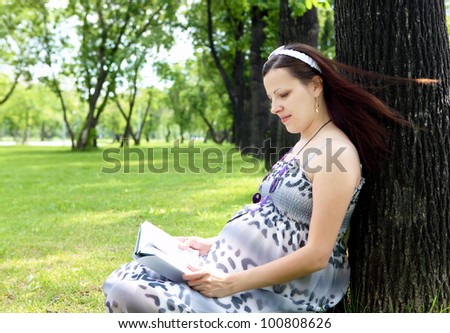 Portrait of pregnant woman reading a book in the park