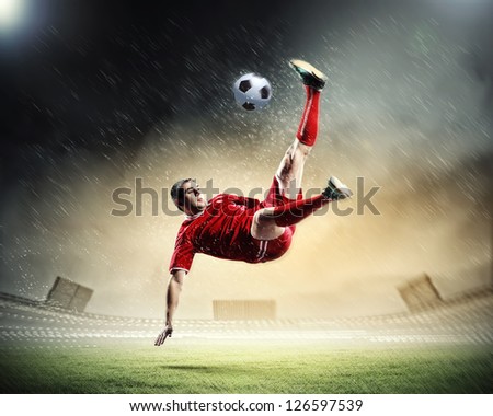 football player in red shirt striking the ball at the stadium under rain