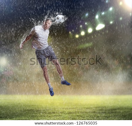 football player in white shirt striking the ball with head at the stadium under the rain
